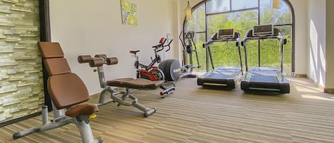 A gym with exercise equipment, a large window, and a view of greenery.