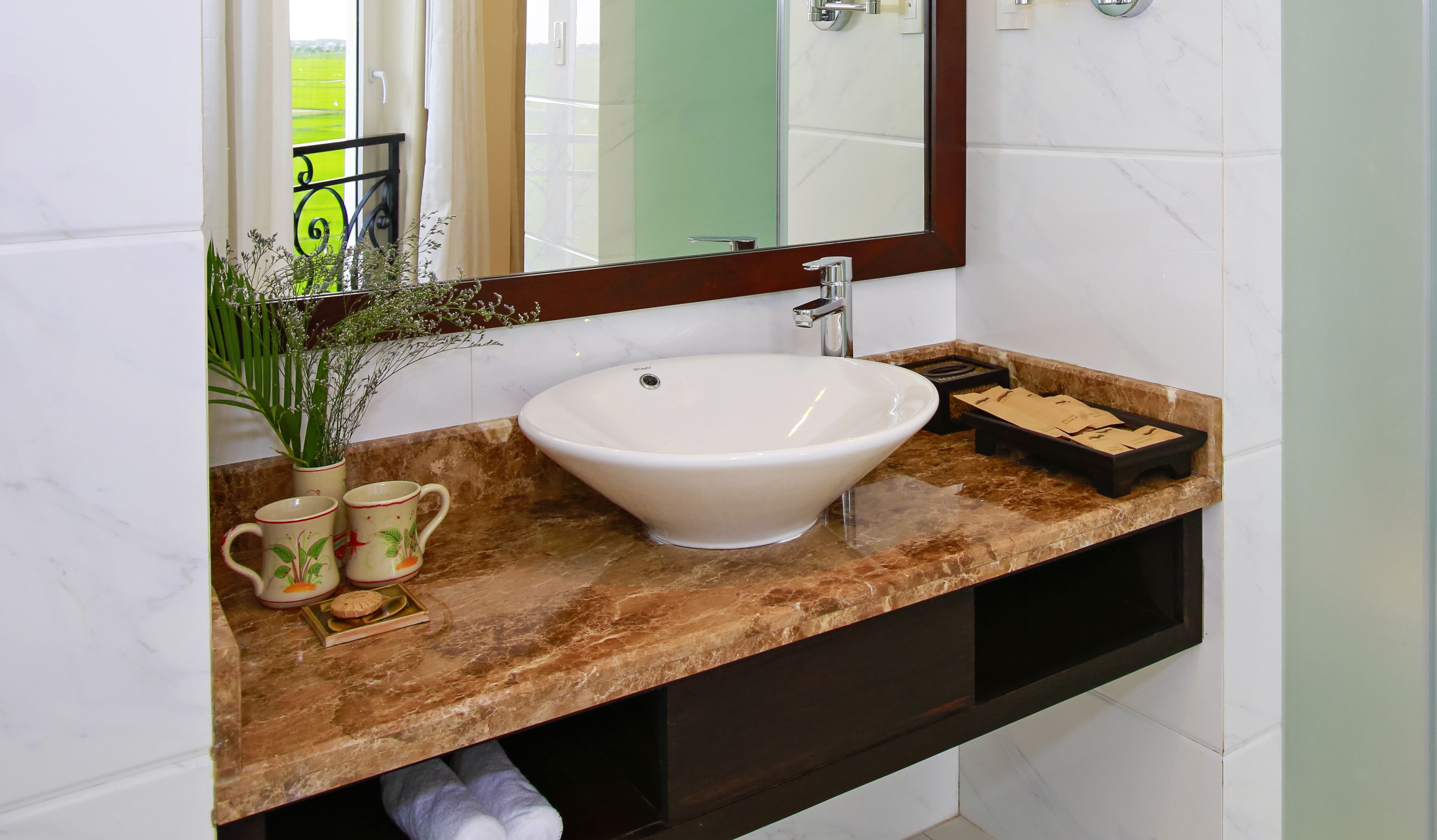 Un bagno con un lavandino bianco, uno specchio e un piano di lavoro in marmo.