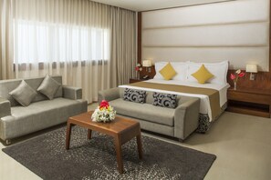 A hotel room with a bed, two sofas, a coffee table, and a nightstand with lamps.
