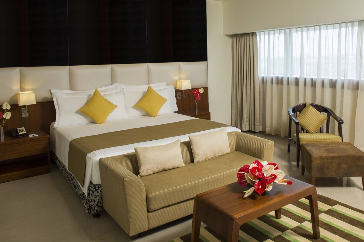 A hotel room with a large bed, a sofa, a chair, a small table, and a window with curtains.