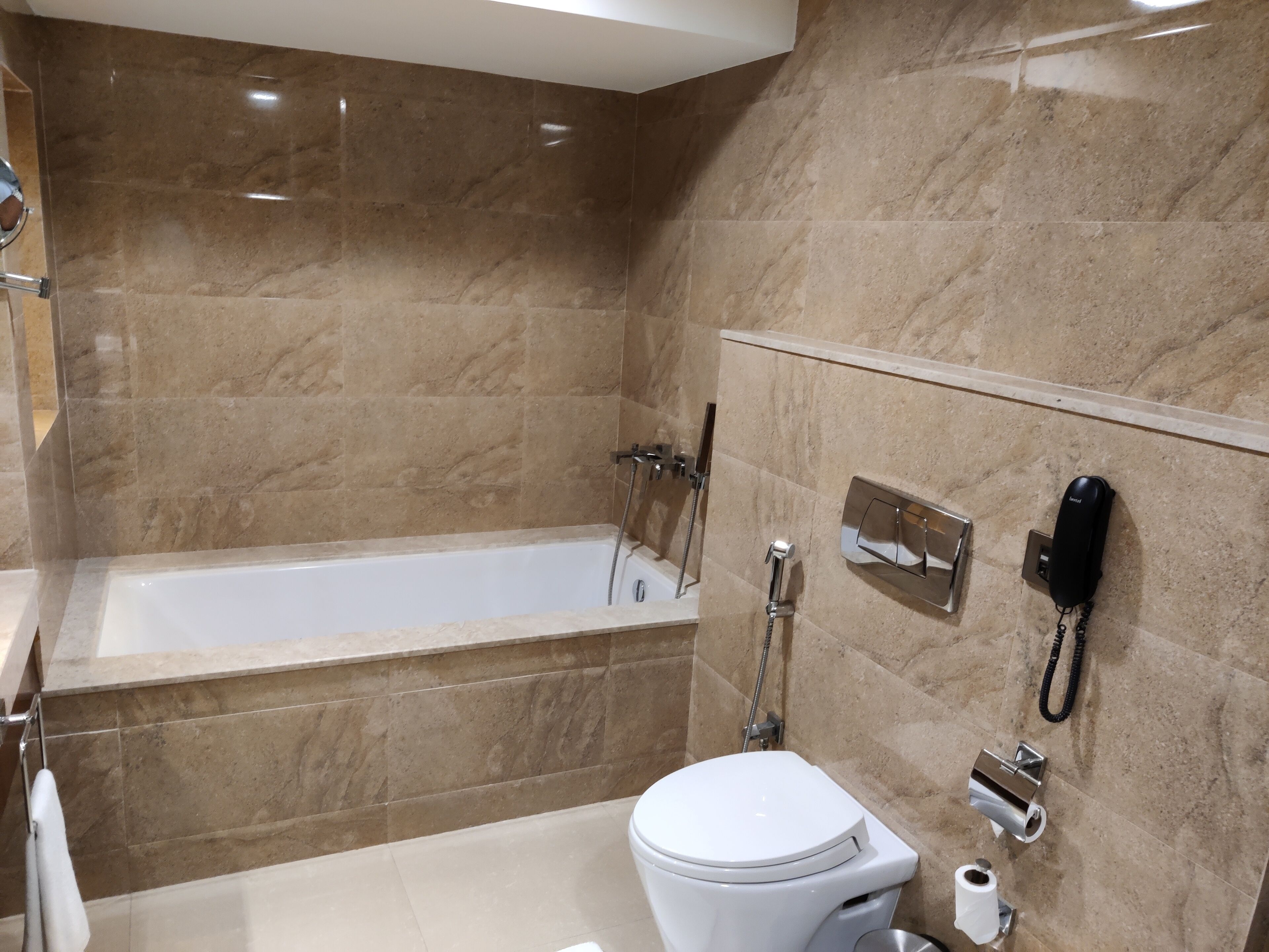 Un baño moderno con bañera, inodoro y teléfono instalado en la pared.