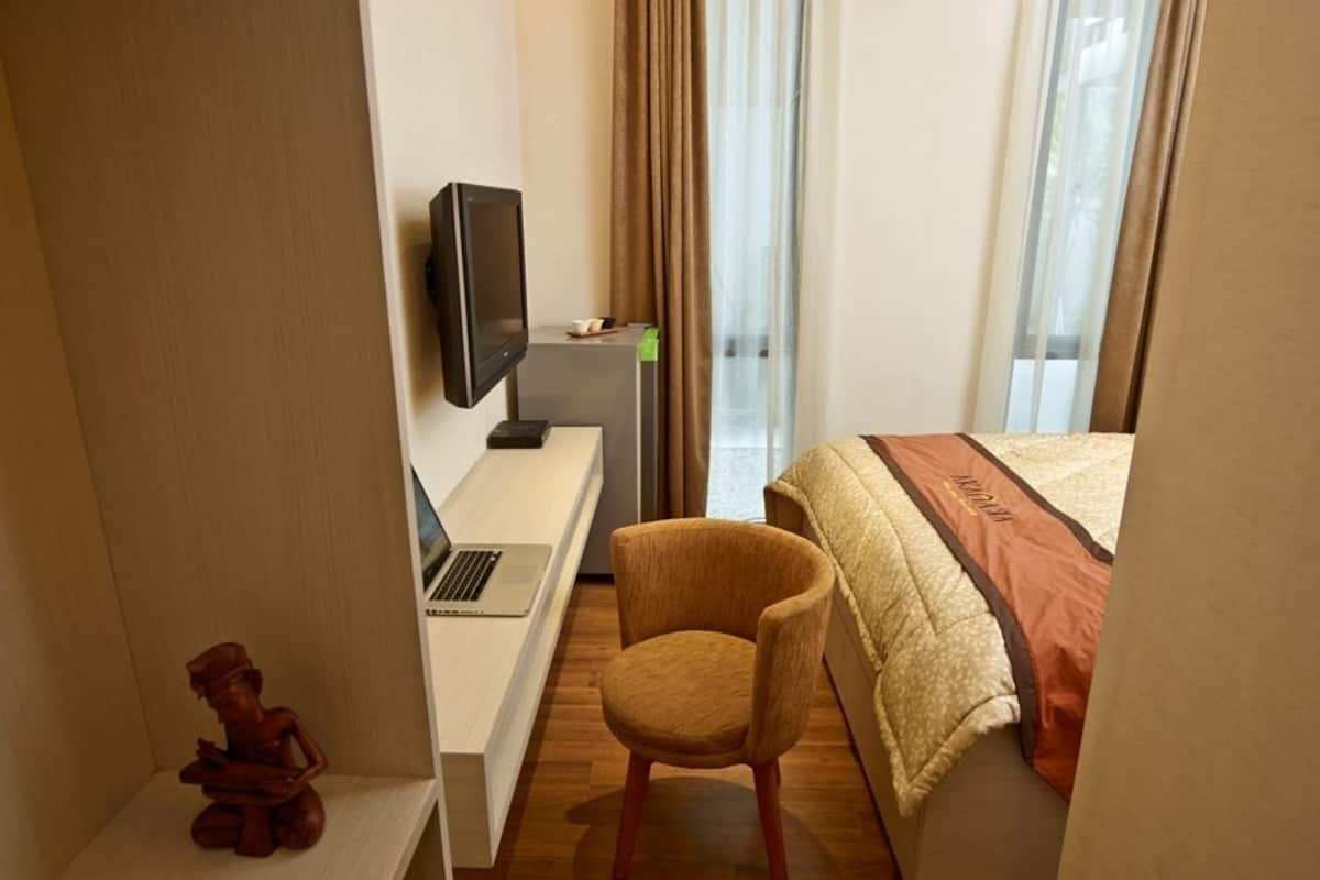 A hotel room with a bed, a desk with a laptop, a television, and a chair.