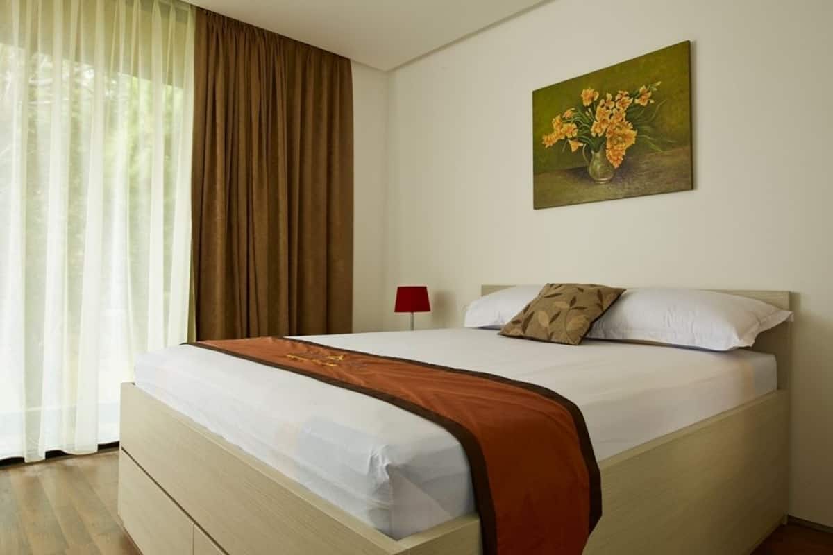 A neatly made bed with a white and brown bedspread, a red lamp on the nightstand, and a painting of flowers on the wall.
