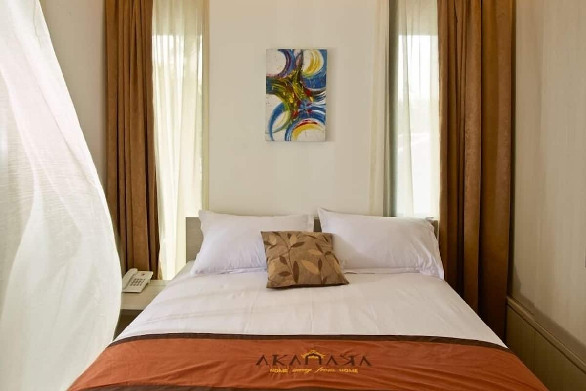 A hotel room with a bed, a painting on the wall, and curtains.