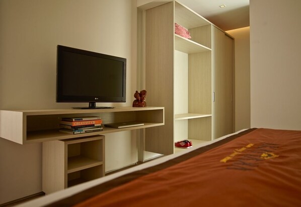 A bedroom with a bed, a TV on a stand, and built-in shelving with books and a small statue. - Akanaka (Jakarta)