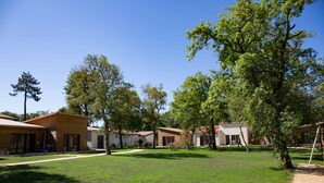 A courtyard with multiple wooden cabins, surrounded by trees and a clear sky.