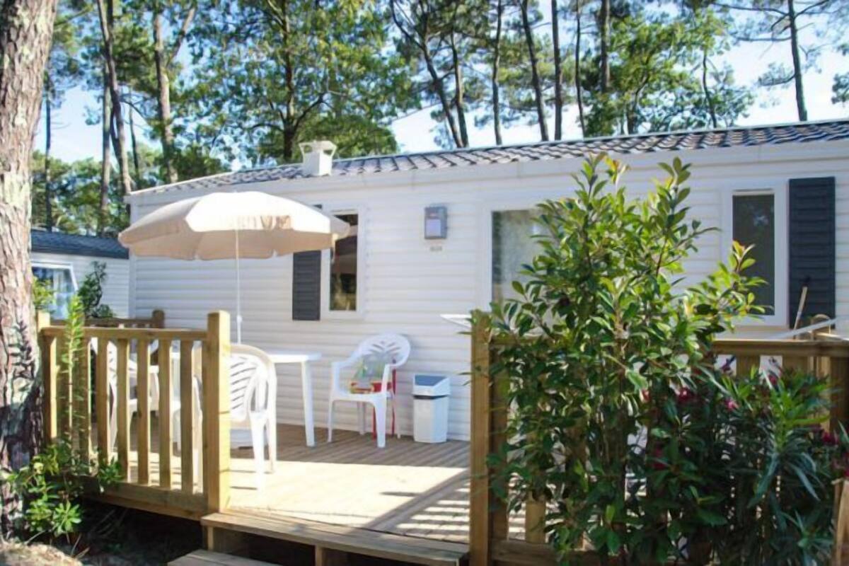 A mobile home with a wooden deck, a white umbrella, and a chair.