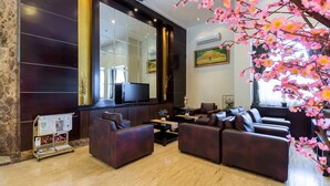 Een moderne woonkamer met donker houten lambrisering, een grote flatscreen televisie, leren banken en een decoratieve bloeiende roze boom.