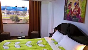 Et hotelværelse med seng, et vindue med gardiner, et billede på væggen og udsigt ud.