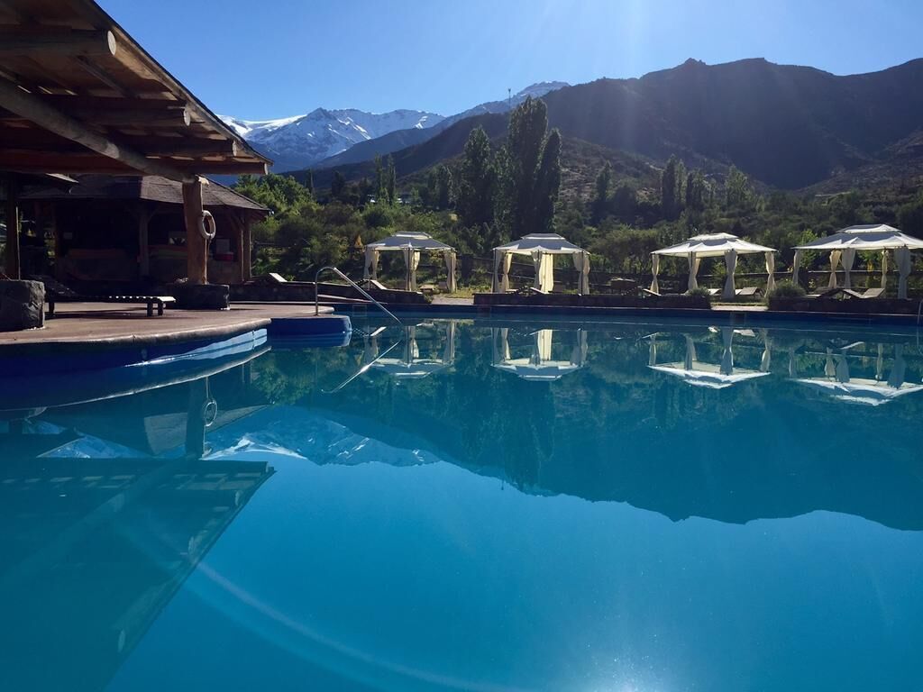 Ein Pool mit klarem Wasser, umgeben von Liegestühlen und Sonnenschirmen, mit Bergen im Hintergrund.