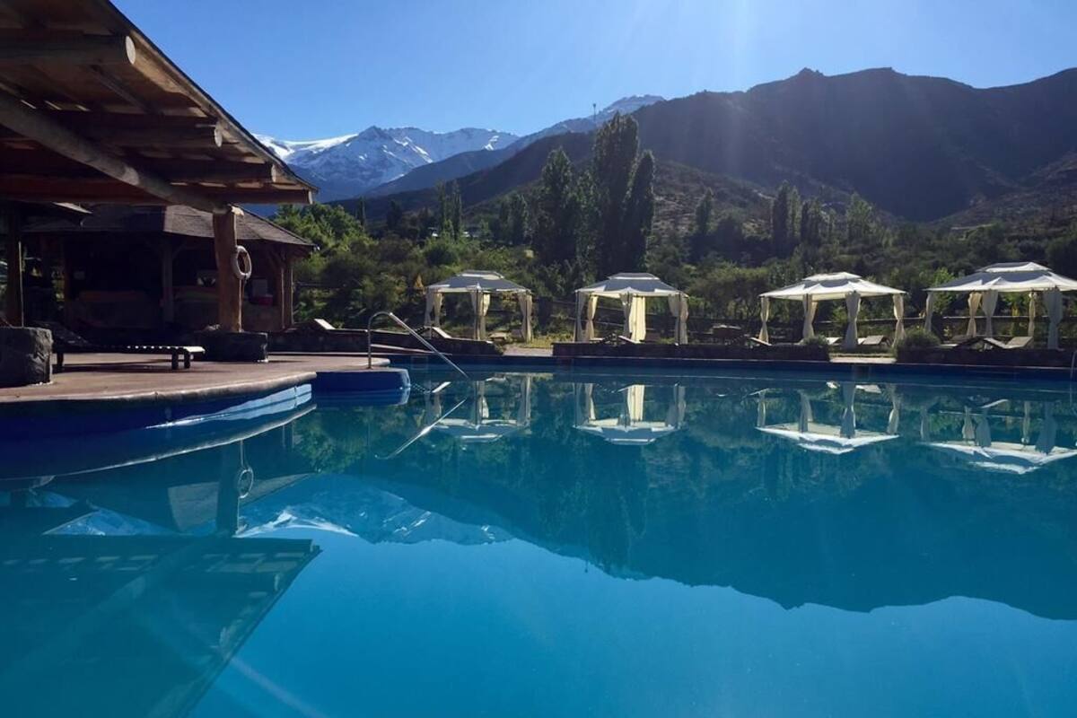 Ein Pool mit klarem Wasser, umgeben von Liegestühlen und Sonnenschirmen, mit Bergen im Hintergrund.