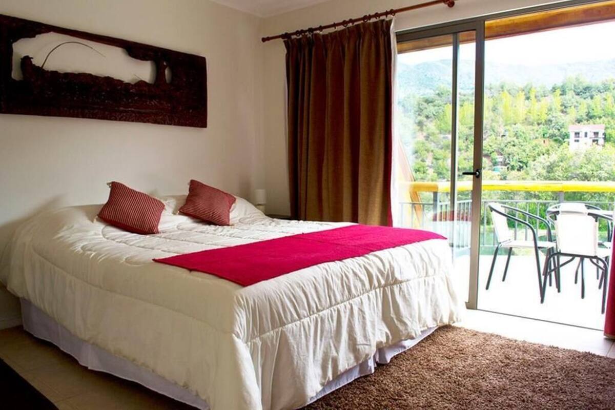 Ein Schlafzimmer mit einem großen Bett, einer roten Tagesdecke und Blick auf einen Balkon mit Stühlen.