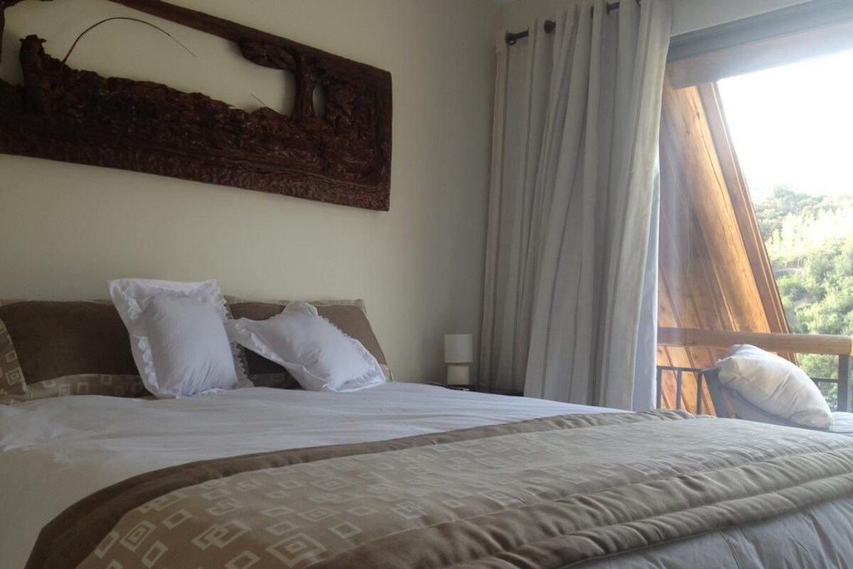 A bedroom with a large bed, a nightstand, a wall-mounted artwork, and a window with curtains.