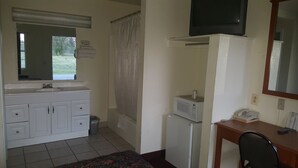 A small, clean room with a white sink, a mirror, a microwave, a small refrigerator, a telephone, and a wooden desk. - American Inn (Mount Vernon)