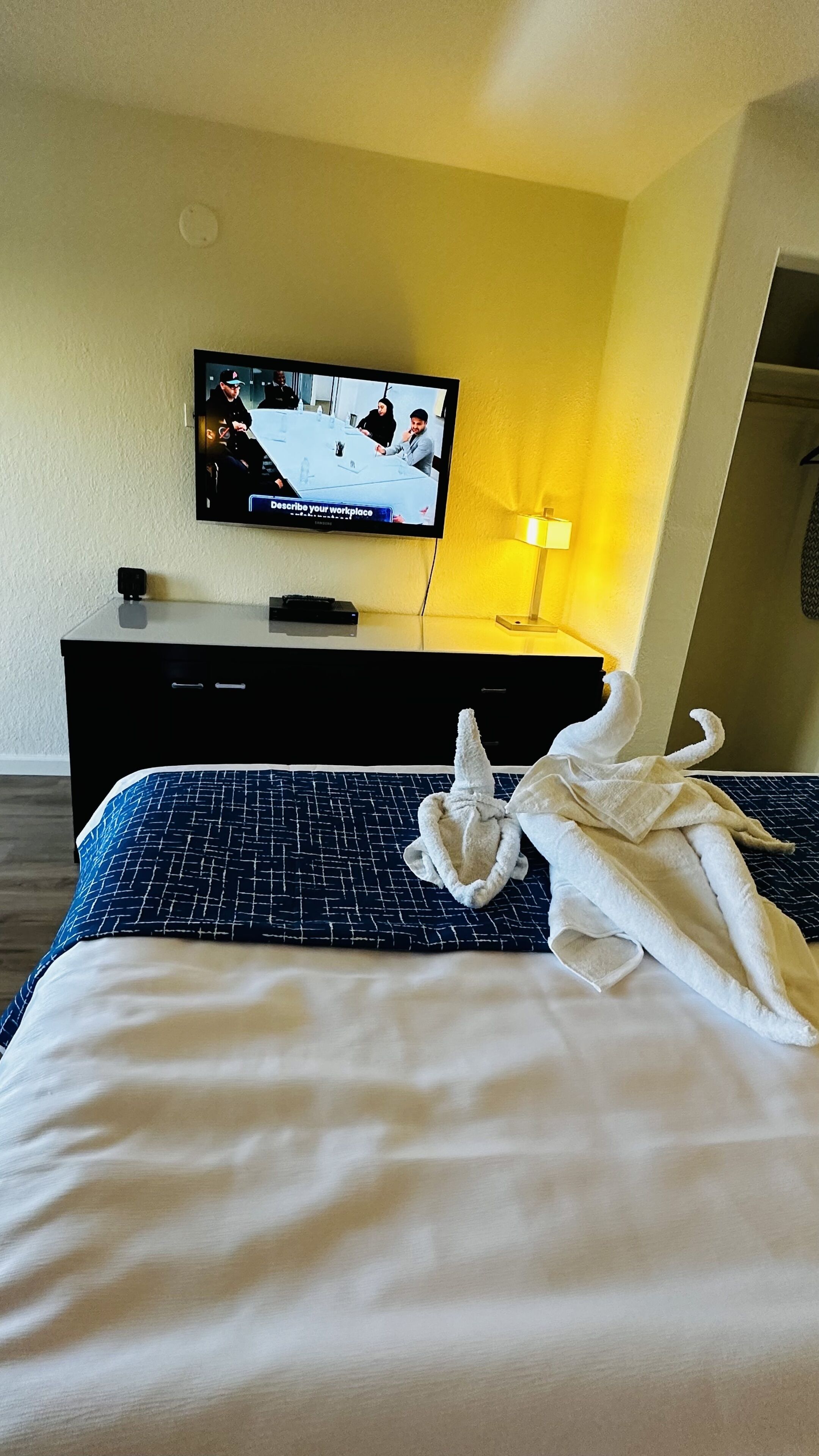Habitació d'hotel amb un llit, un televisor penjat a la paret, un escriptori amb una làmpada i una bata sobre el llit.
