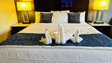 Habitación de hotel con una cama grande, dos lámparas de noche, cabecera con un cuadro y suelo de madera.