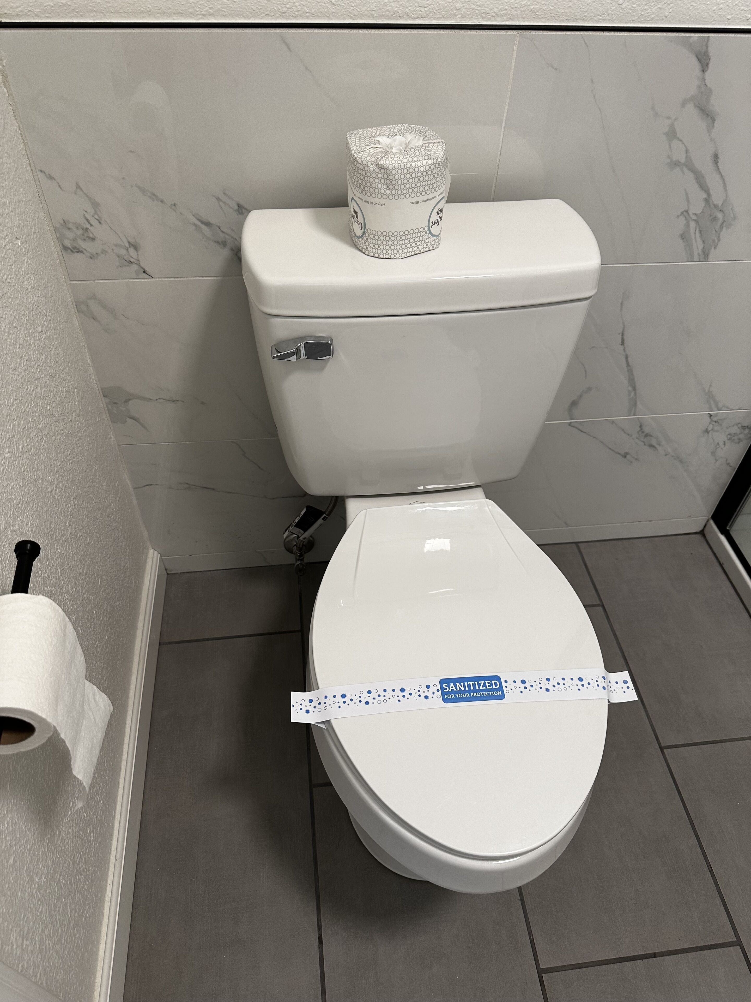 Un inodoro con un sujetapapeles a la izquierda y un rollo de papel higiénico en el suelo.