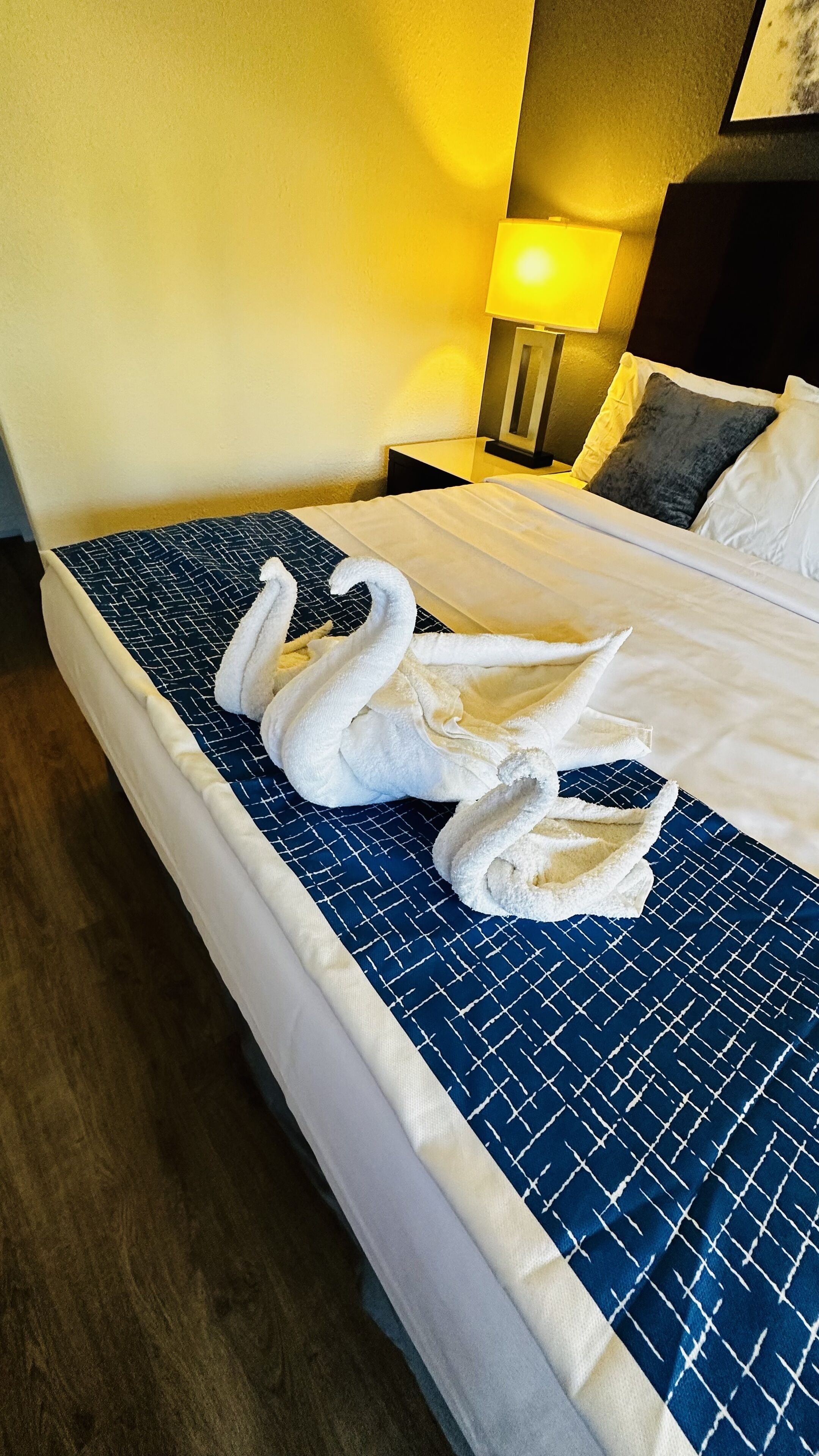 A neatly made bed with a blue patterned bedspread and two white towels arranged in a swan shape.