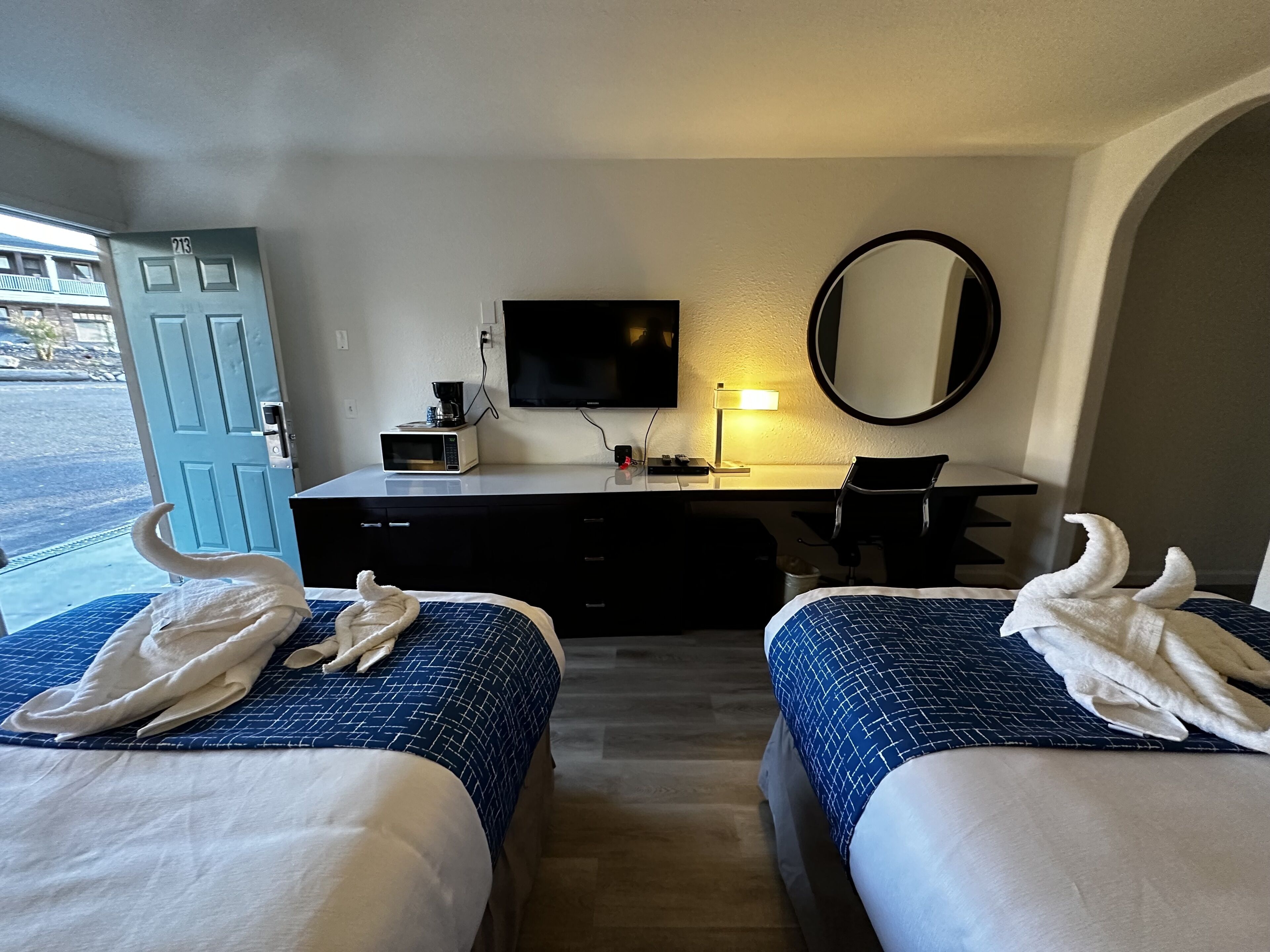 A hotel room with two beds, a desk, a TV, a microwave, and a mirror.