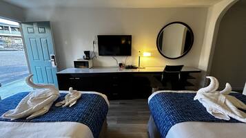 Et hotelværelse med to senge, et skrivebord, et fjernsyn, en mikrobølgeovn og et spejl.
