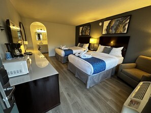 Habitación de hotel con dos camas, un escritorio con cafetera, un sofá y obras de arte en las paredes.