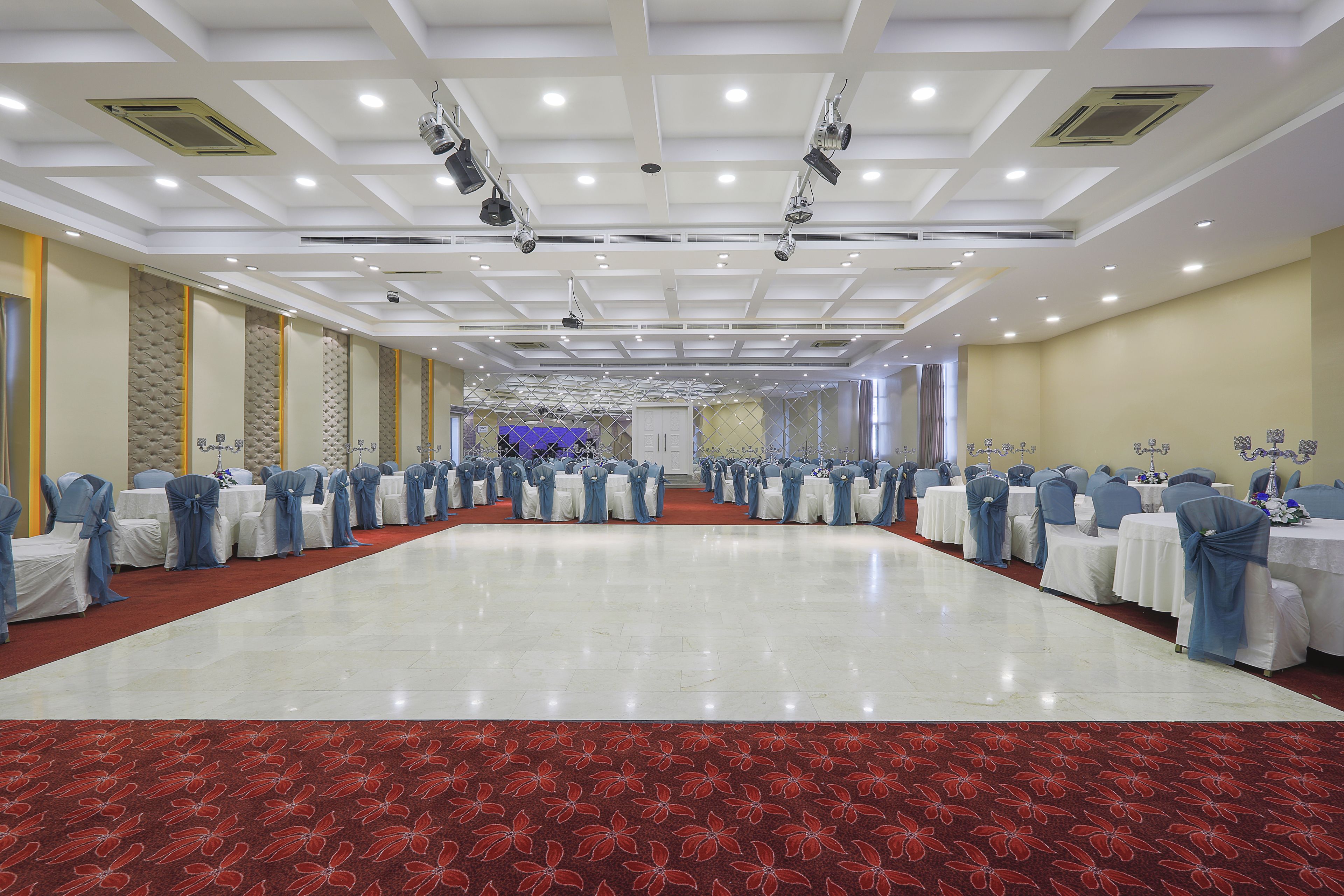 A spacious hall with rows of tables and chairs, a red carpet, and a stage at the far end.