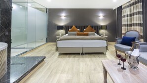Une chambre d’hôtel moderne dotée d’un grand lit, d’un coin salon avec un canapé et des fauteuils, d’une douche en verre et d’un plancher en bois.