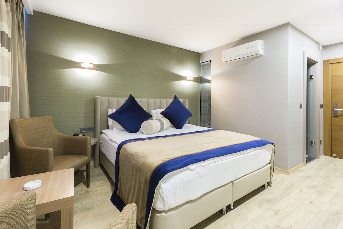 A hotel room with a bed, a chair, a table, and an air conditioning unit.