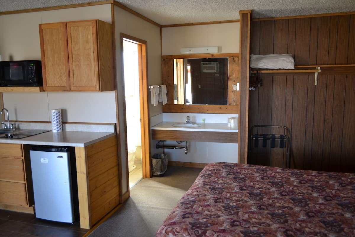 A compact room with a kitchenette, a bed, and a wooden wardrobe.