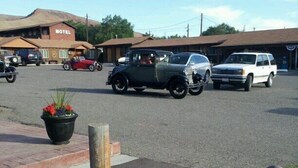 A motel with a sign, a parking lot with vintage cars, and a landscaped area with rocks and plants. - The Village Inn Motel and Restaurant (Challis)