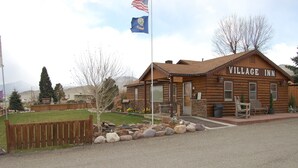 A log cabin-style building labeled "VILLAGE INN" with a flagpole, a small front porch, and a stone pathway leading to the entrance. - The Village Inn Motel and Restaurant (Challis)