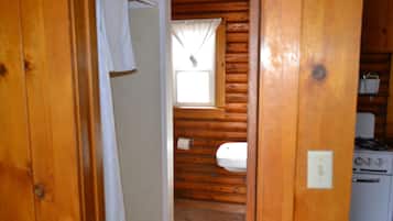 Interior de cabana de madeira com banheiro, janela e fogão.