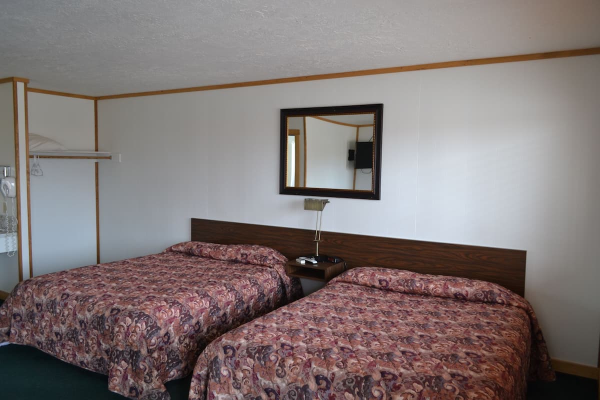 A room with two beds, a wooden headboard, a nightstand, a mirror, and a coat rack.