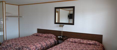 A room with two beds, a wooden headboard, a nightstand, a mirror, and a coat rack.