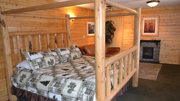 A log cabin-style bedroom with a four-poster bed, wooden walls, a fireplace, and a mounted plant. - The Village Inn Motel and Restaurant (Challis)