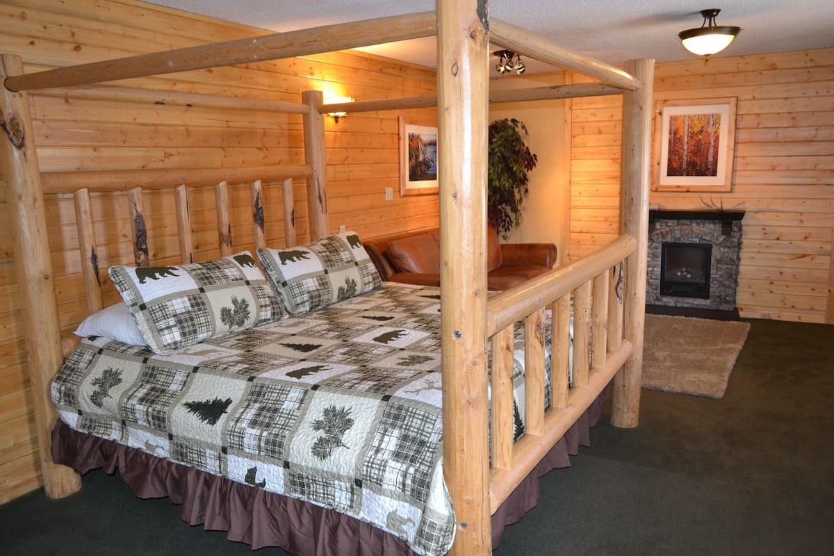 A log cabin-style bedroom with a four-poster bed, wooden walls, a fireplace, and a mounted plant.