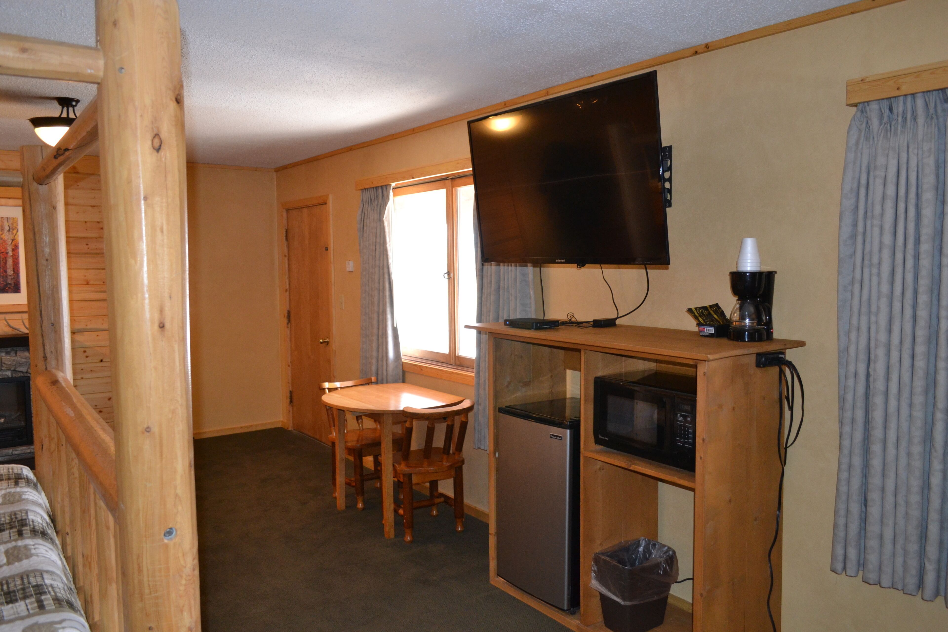 Een kleine kamer met een kitchenette, een televisie, een kleine koelkast en een eethoek met een tafel en stoelen.