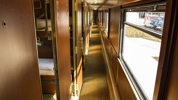 A train compartment with wooden walls, a patterned floor, and a window with a view of the outside. - Train Lodge Amsterdam - Hostel (Amsterdam)