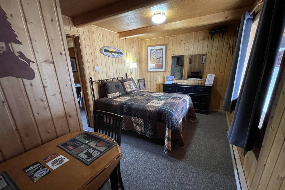A wooden cabin room with a bed, a desk, and a dresser.