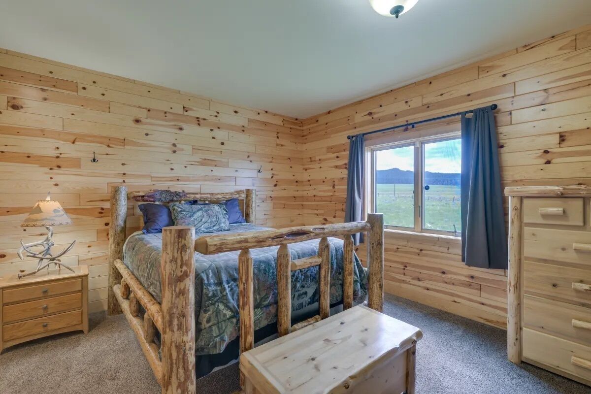 A wooden cabin bedroom with a bed, nightstand, dresser, and a window with a view of the outdoors.