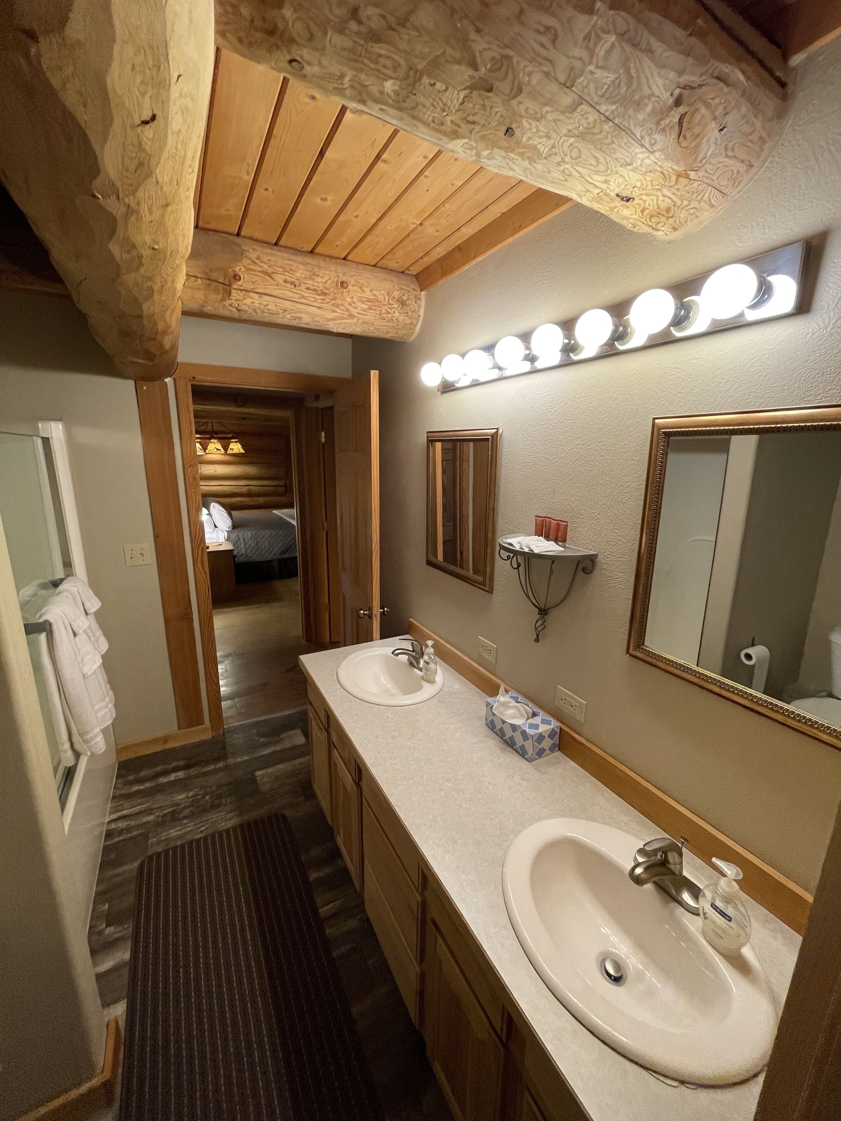 Een badkamer met twee wastafels, een spiegel en een wastafelmeubel. Er is een houten plafond en een lamp boven de spiegel.