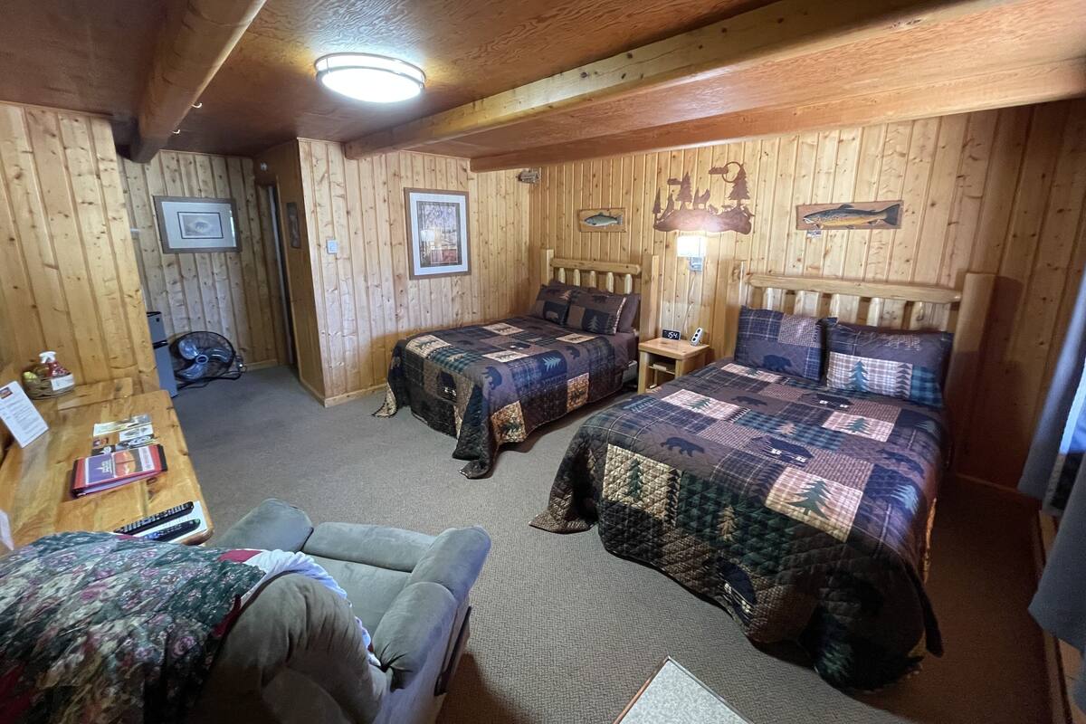 A wooden cabin room with two beds, a desk, and a chair.
