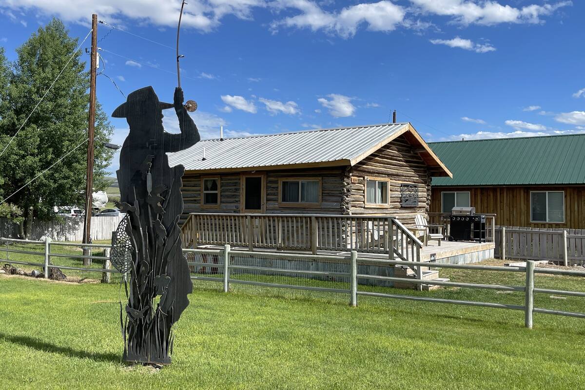 A rustic log cabin with a metal roof, a wooden deck, and a fenced yard.