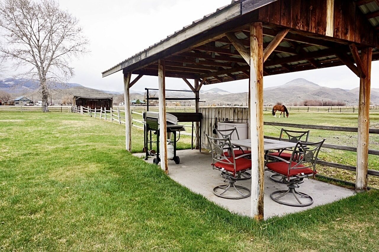 Un espacio al aire libre cubierto con mesas y sillas, una valla de madera y un caballo al fondo.