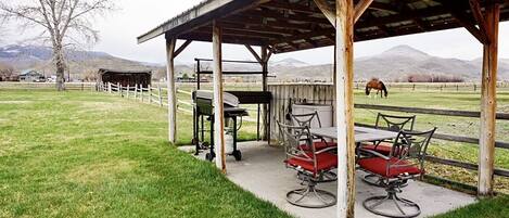 Un espacio al aire libre cubierto con mesas y sillas, una valla de madera y un caballo al fondo.