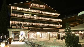 Un hotel con múltiples balcones decorados con luces, un patio cubierto de nieve y un letrero que indica que es un hotel.