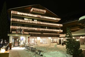 Un hotel con múltiples balcones decorados con luces, un patio cubierto de nieve y un letrero que indica que es un hotel.
