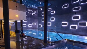 A modern indoor swimming pool with geometric light patterns on the walls and a clear water surface. - Zermatt Budget Rooms at Alpen Resort, Spa & Dining (Zermatt)