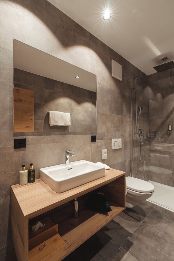 A modern bathroom with a large mirror, a white sink, a shower, and a wooden vanity. - Zermatt Budget Rooms at Alpen Resort, Spa & Dining (Zermatt)