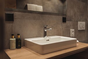 Un baño con un lavamanos rectangular blanco, dos botellas de líquido, un espejo y una toalla.
